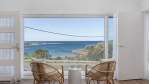 Varanda com cadeiras de vime e uma mesa pequena, com vista para a costa e céu claro.