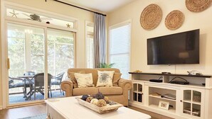 Ett vardagsrum med en beige soffa, ett vitt soffbord, en tv och en öppen spis.