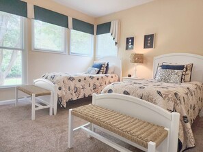 Een slaapkamer met twee bedden, een bankje en een lamp.