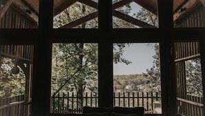 A room with a large window offering a view of a forested area and a distant building. - La Cabane De La Saône, Lyon Country House (Caluire et Cuire)