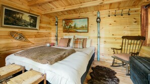 A wooden cabin bedroom with a bed, a chair, a painting, and a coat rack. - La Cabane Du Trappeur   Lyon Country House (Caluire et Cuire)