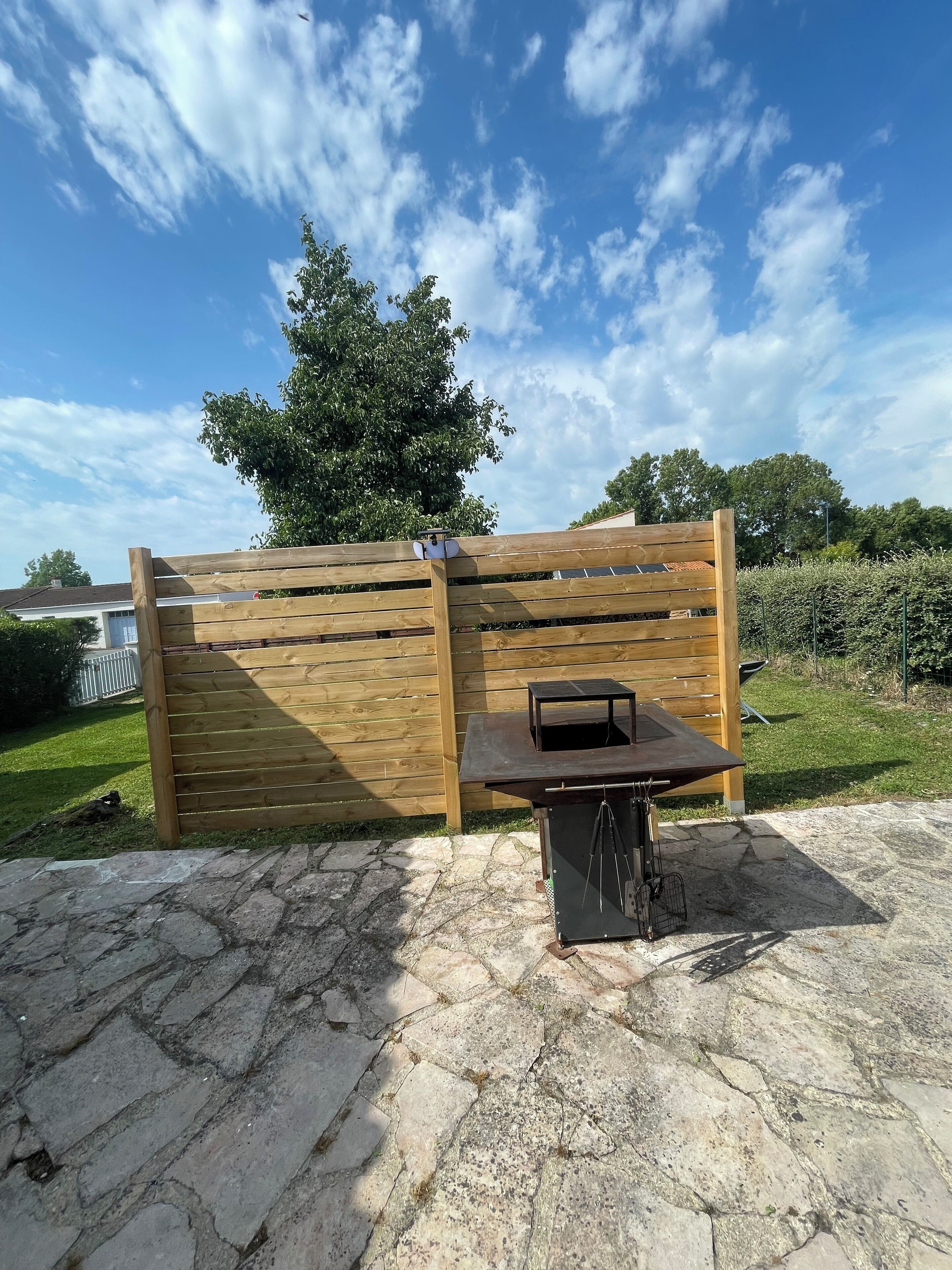 En uteplats med ett stengolv, ett trästaket och en grill.