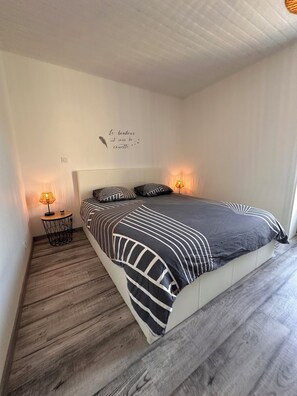 Une chambre à coucher avec un lit, deux lampes de chevet, un élément de décoration murale et une petite table ronde.