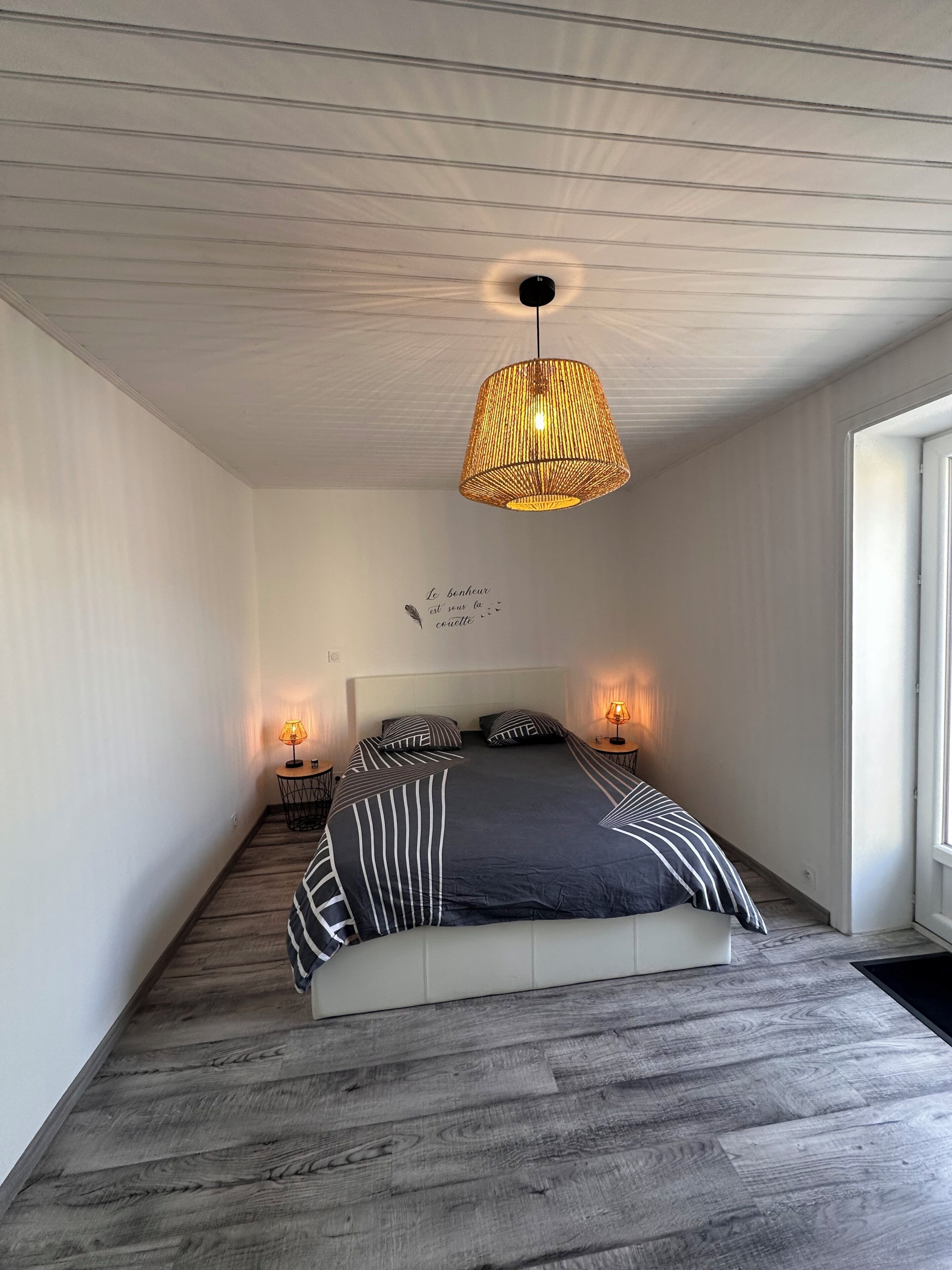 Un dormitorio con cama, dos lámparas de noche, un candelabro colgante y una pared con una cita decorativa.
