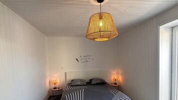 Un dormitorio con cama, dos lámparas de noche, un candelabro colgante y una pared con una cita decorativa.