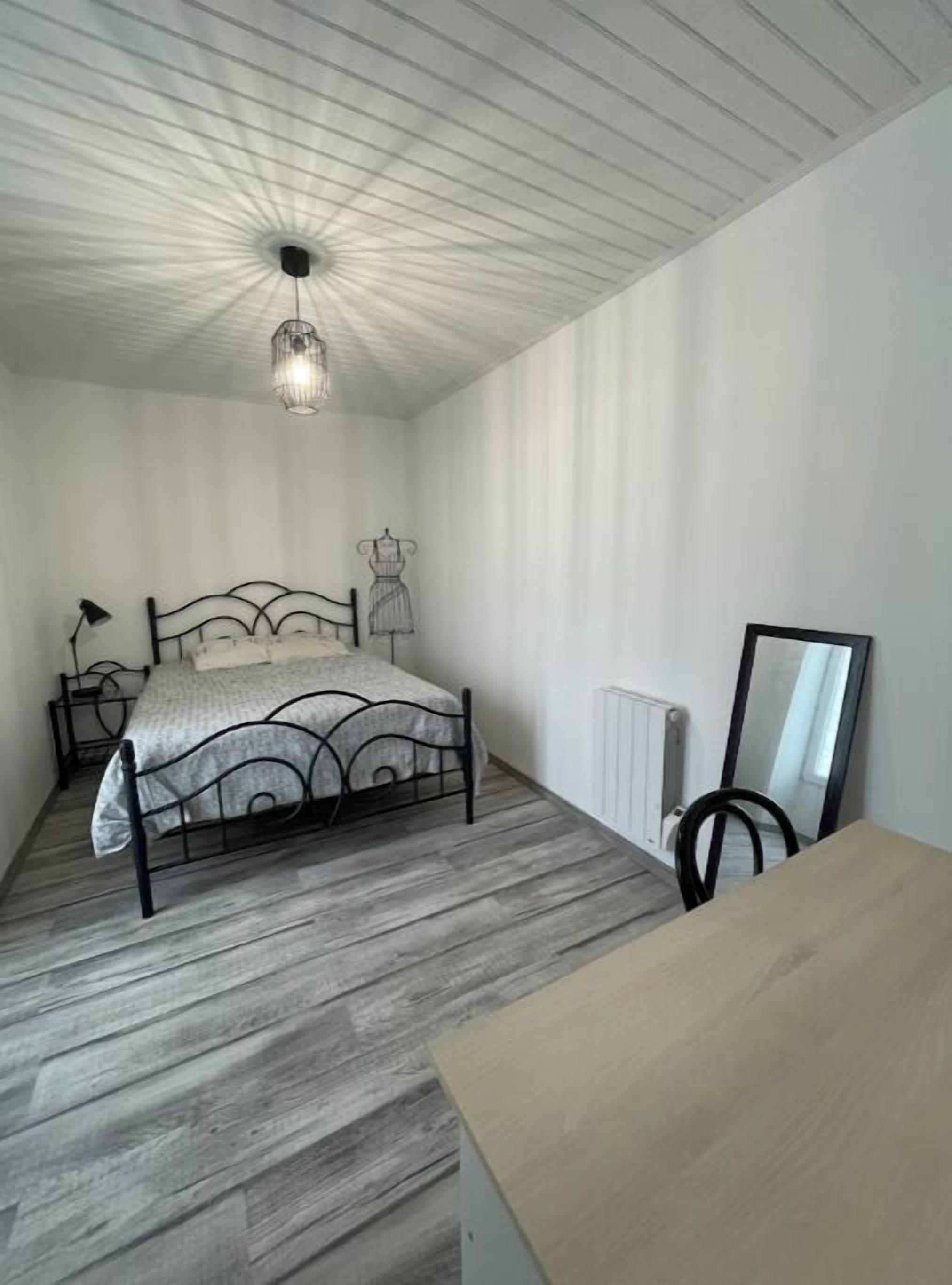 Une chambre à coucher comprenant un lit, une commode, un radiateur, un miroir et un luminaire suspendu.