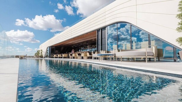 Een modern hotel met een zwembad, terras en een grote glazen gevel die de lucht weerspiegelt.