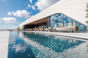 A modern hotel with a pool, outdoor seating, and a large glass facade reflecting the sky. - This apartment is a 1 bedroom(s), 1 bathrooms, located in St. Julian's, null. (St. Julian's)
