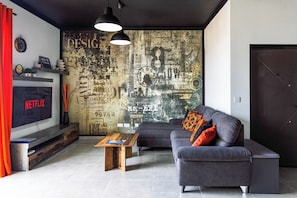 A modern living room with a large wall mural, a flat-screen TV, a sofa, and a coffee table.