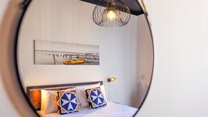 A bedroom with a bed, pillows, a wall-mounted picture, and a unique circular mirror.