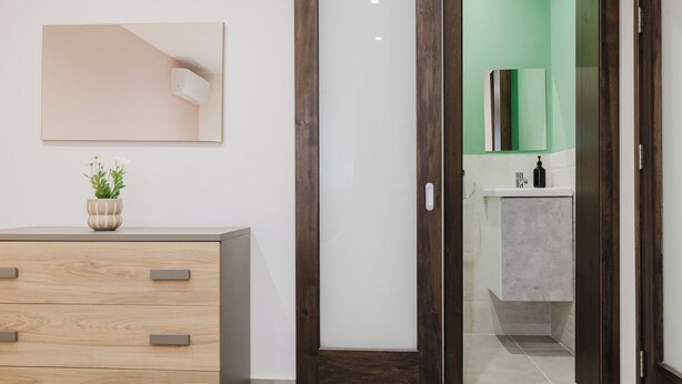 A modern bathroom with a green wall, a white sink, and a wooden vanity with drawers.