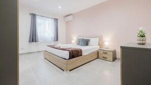 A modern bedroom with a wooden bed, bedside tables, a nightstand, a desk, and a potted plant.