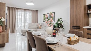 Un salon moderne avec un coin repas, comprenant un canapé, une table à manger dressée avec des assiettes et des verres, et une bouteille de vin.