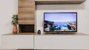 Un téléviseur à écran plat fixé sur un meuble blanc, avec un panneau décoratif en bois au-dessus.