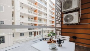 Un balcon avec une table préparée pour le petit-déjeuner, comprenant des croissants et du café, donnant sur un immeuble à plusieurs étages doté de balcons.
