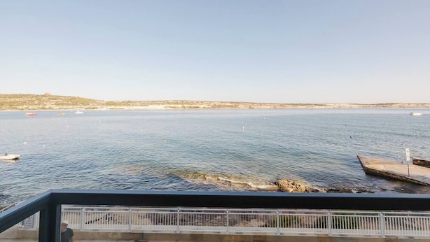 Blick auf die Küste vom Balkon mit Geländer, felsige Uferlinie und Boote im Wasser.