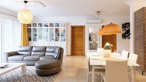 A modern living room with a leather sofa, a dining table set for four, and a bookshelf filled with books. - 102 Seafront 3Bed Sliema with pool by Homely (Tas-Sliema)
