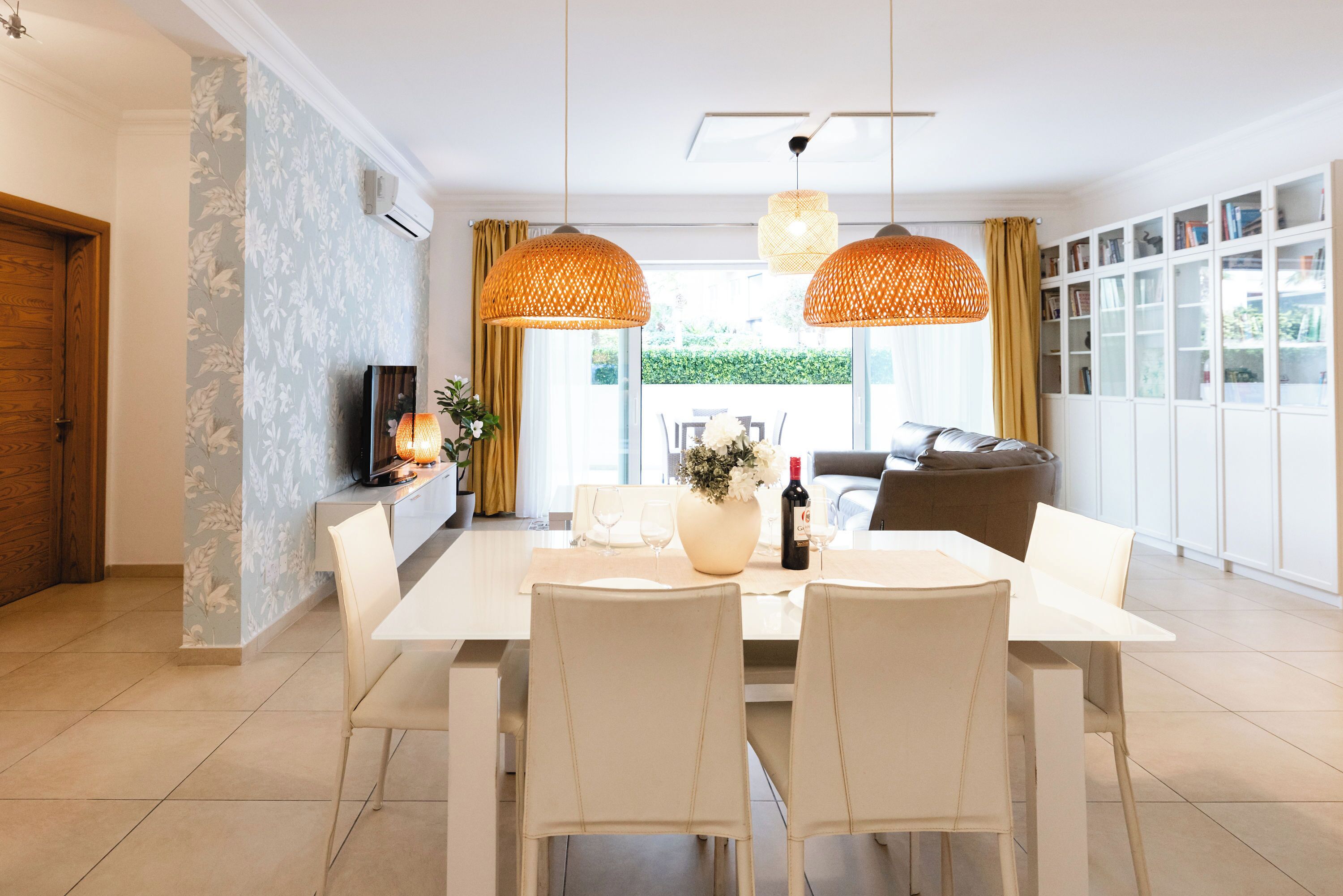 A dining area with a white table, four chairs, a vase with flowers, and two hanging lamps.