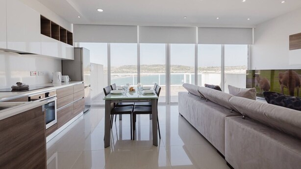 A modern kitchen with a dining area and a sofa, large windows with a view of the sea, and a flat-screen TV. - This apartment is a 2 bedroom(s), 1 bathrooms, located in Il-Mellieħa, null. (Il-Mellieħa)