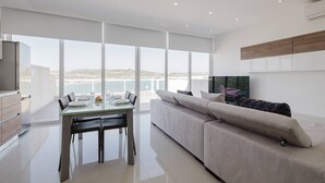 A modern living room with a large window, a dining area, and a sofa. - This apartment is a 2 bedroom(s), 1 bathrooms, located in Il-Mellieħa, null. (Il-Mellieħa)