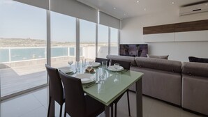 A modern dining area with a table set for two, a sofa, and a TV on the wall. - This apartment is a 2 bedroom(s), 1 bathrooms, located in Il-Mellieħa, null. (Il-Mellieħa)