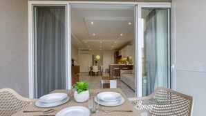 A dining area with a table set for four, a kitchen in the background, and a sliding glass door leading to a balcony.