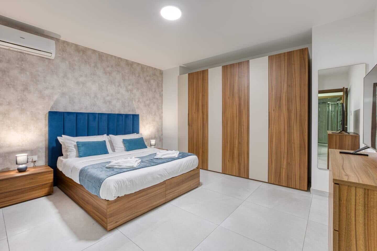 A modern bedroom with a large bed, wooden wardrobe, and a flat-screen TV.