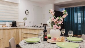A modern kitchen with a dining area, featuring a granite countertop, a clock, a vase with flowers, and a bottle of wine.