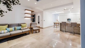 A modern living room with a sofa, armchairs, and a dining area with bar stools.