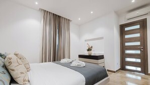 A modern bedroom with a large bed, a bedside table with a vase, and a wooden door.