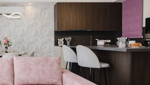 Una cocina moderna con armarios de madera oscura, salpicadero de mármol y una zona de bar. En primer plano, hay un sofá rosa y dos sillas blancas.