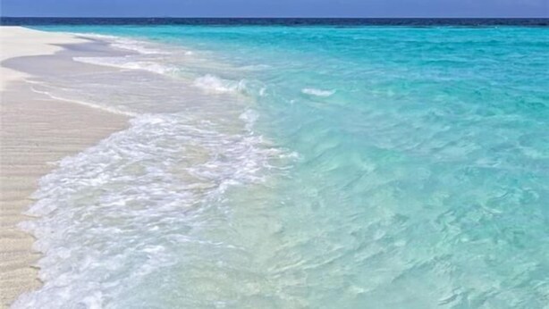 Een strand met helder turquoise water en wit zand.