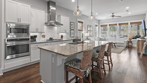 Een moderne keuken met witte kasten, roestvrijstalen apparatuur en een groot kookeiland met barkrukken.