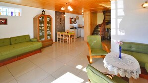 Uma sala de estar ampla com teto de madeira, sofás verdes, um espaço de refeições com cadeiras e uma escada que leva a outro andar.