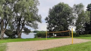 Uma rede de voleibol num parque com um lago e árvores ao fundo.