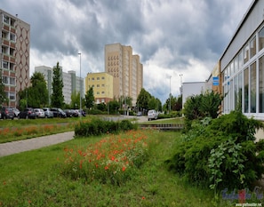 A residential area with apartment buildings, a parking lot, and a garden with red flowers. - Doppelhaushalfte, Schonwalde (Schönwalde-Glien)