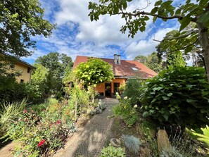 A house with a red-tiled roof, surrounded by a garden with various plants and a cobblestone path leading to the entrance. - Doppelhaushalfte, Schonwalde (Schönwalde-Glien)