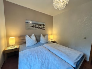 A hotel room with a bed, two bedside lamps, a nightstand, a wall-mounted picture, and a decorative ceiling light fixture. - Doppelhaushalfte, Schonwalde (Schönwalde-Glien)