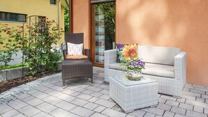 En patio med fletningsmøbler, heriblandt en stol og en sofa, samt et lille bord med en blomstervase.