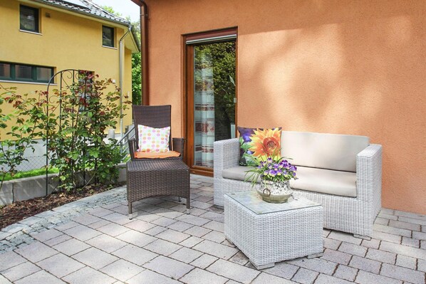 A patio with wicker furniture, including a chair and a sofa, and a small table with a flower vase. - Doppelhaushalfte, Schonwalde (Schönwalde-Glien)