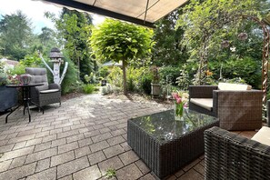 An outdoor patio with wicker furniture, a glass table, and a variety of plants. - Doppelhaushalfte, Schonwalde (Schönwalde-Glien)