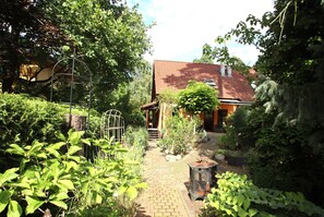 A garden pathway leading to a house with a red roof, surrounded by lush greenery and various plants. - Doppelhaushalfte, Schonwalde (Schönwalde-Glien)