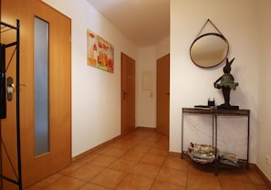 A hallway with wooden doors, a wall-mounted mirror, a small table with a basket of magazines, and a painting on the wall. - Doppelhaushalfte, Schonwalde (Schönwalde-Glien)