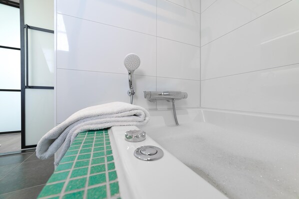 A bathroom with a bathtub, a showerhead, and a towel on the edge.