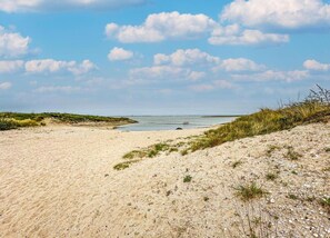 A sandy beach with dunes and a calm sea under a partly cloudy sky.