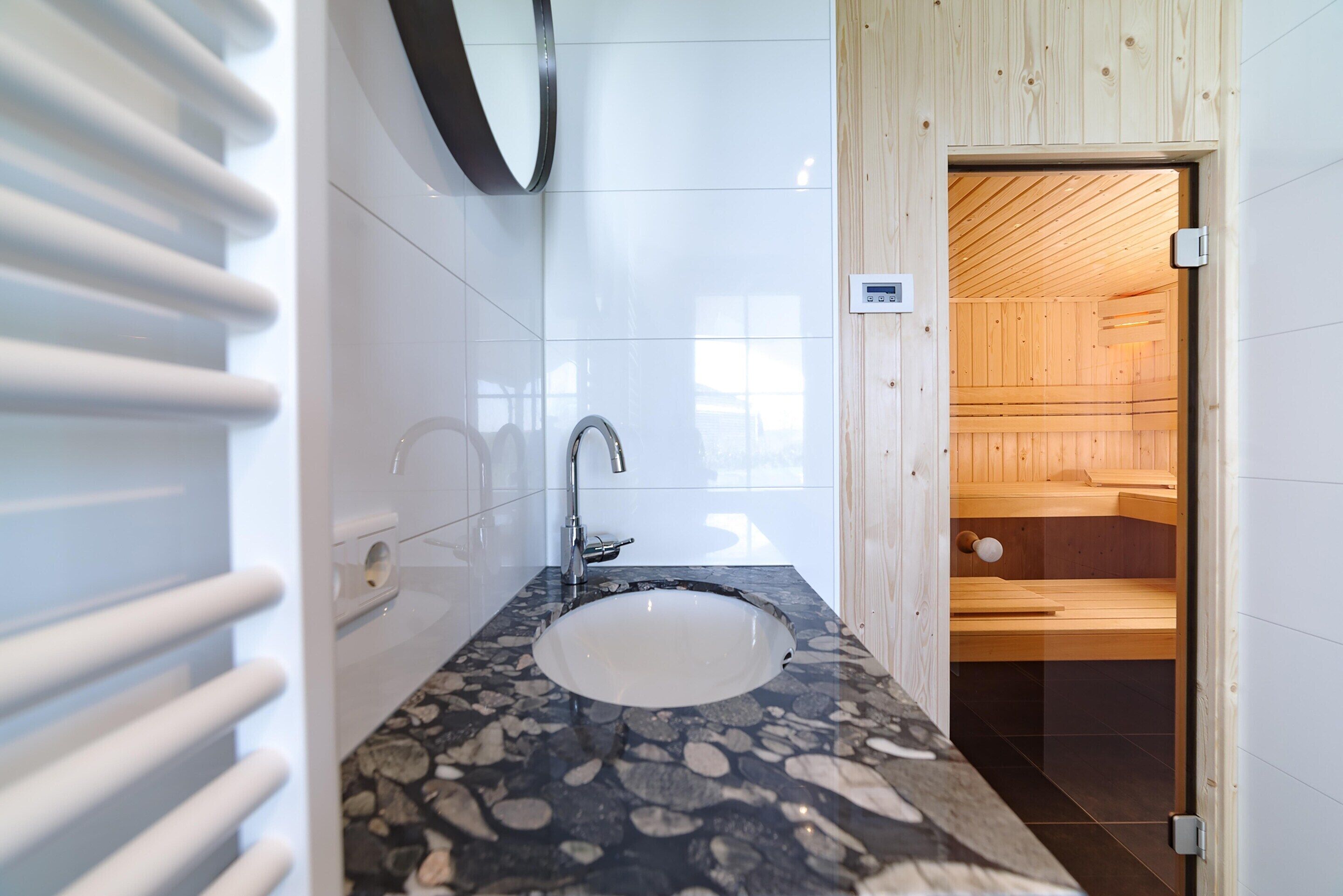 Un baño moderno con un lavabo de piedra, un espejo y una sauna visible a través de una puerta abierta.