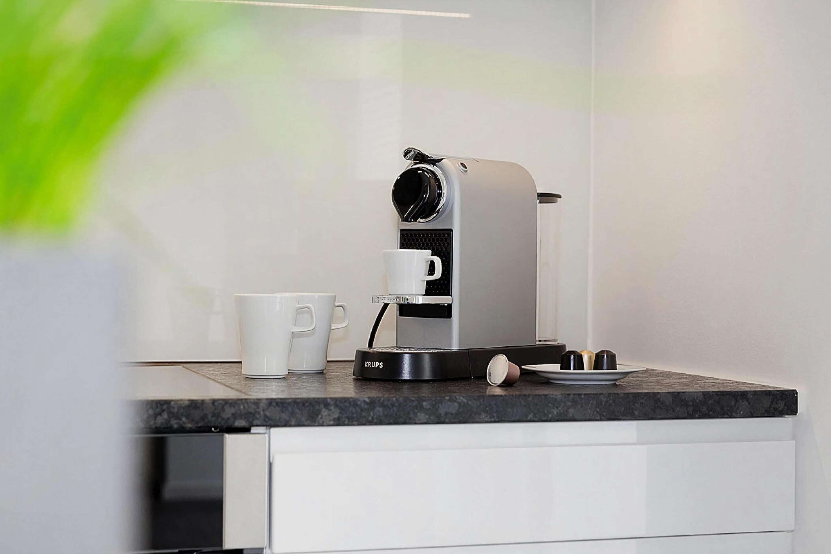 Eine moderne Kaffeemaschine auf einer Küchenarbeitsplatte, zusammen mit einer weißen Tasse und einem Tablett mit Kaffeetassen.