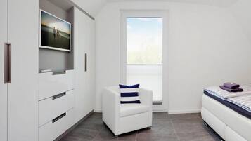 A modern bedroom with a white wardrobe, a white armchair with a striped pillow, a bed with a striped duvet, and a large window with a view of trees.