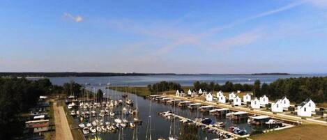 A marina with boats docked, a row of white buildings, and a clear view of the water and distant land.