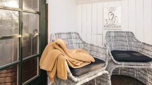 A room with two wicker chairs, one with a dark cushion and the other with a light cushion. A beige blanket is draped over the chair with the dark cushion. A sign on the wall reads "KUNSTLADEN" with a penguin illustration. - Hotel Fanobad With Free Water Park Access (Fano)